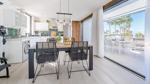 Una cocina moderna con comedor, ventanas amplias y vista a palmeras.