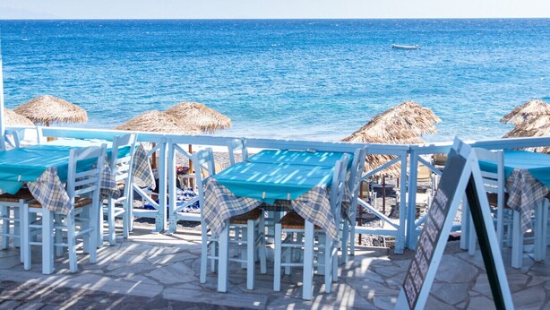 Un restaurante frente al mar con terraza, sombrillas de paja y vistas al océano.