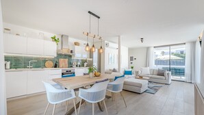 Una cocina moderna con armarios blancos, una mesa de comedor de madera y lámparas colgantes.