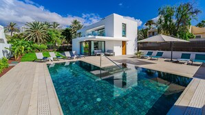Un área de piscina moderna con agua cristalina, rodeada de sillas de descanso y un edificio contemporáneo.