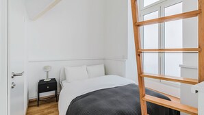 A minimalist bedroom with a bed, bedside table, lamp, and a wooden ladder. - Blueground | Leopoldstadt, furniture & decor (Vienna)