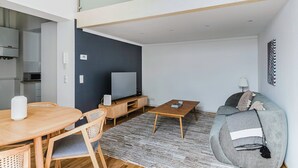 A modern living room with a dining area, a grey sofa, a wooden coffee table, and a flat-screen TV. - Blueground | Leopoldstadt, furniture & decor (Vienna)