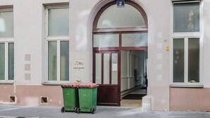 A building with a large arched entrance, a sign above the door, and two green dumpsters on the sidewalk. - Blueground | Leopoldstadt, furniture & decor (Vienna)