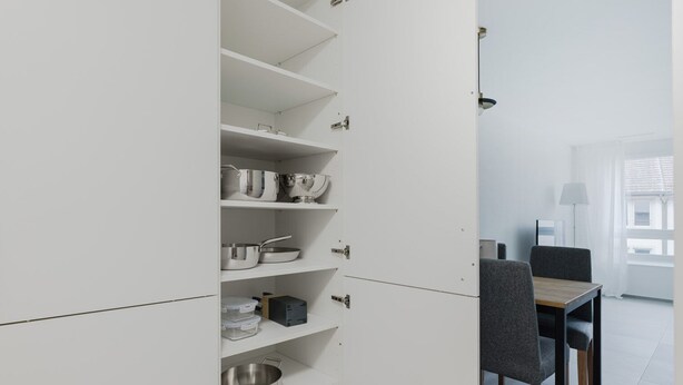 Ett modernt kök med vita köksluckor, köksredskap i rostfritt stål och en matplats med bord och stolar.