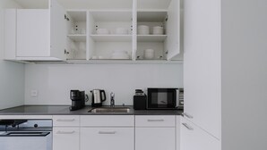 Ett modernt kök med vita skåp, en diskho i rostfritt stål, en kaffebryggare, en vattenkokare och en mikrovågsugn.
