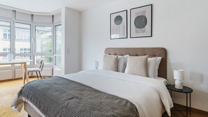 Une chambre d’hôtel moderne avec un grand lit, un bureau et deux œuvres d’art encadrées accrochées au mur.