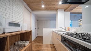 A modern kitchen with a wooden floor, white cabinets, a gas stove, and a microwave. - ZABO HILLS 305 (Sapporo)