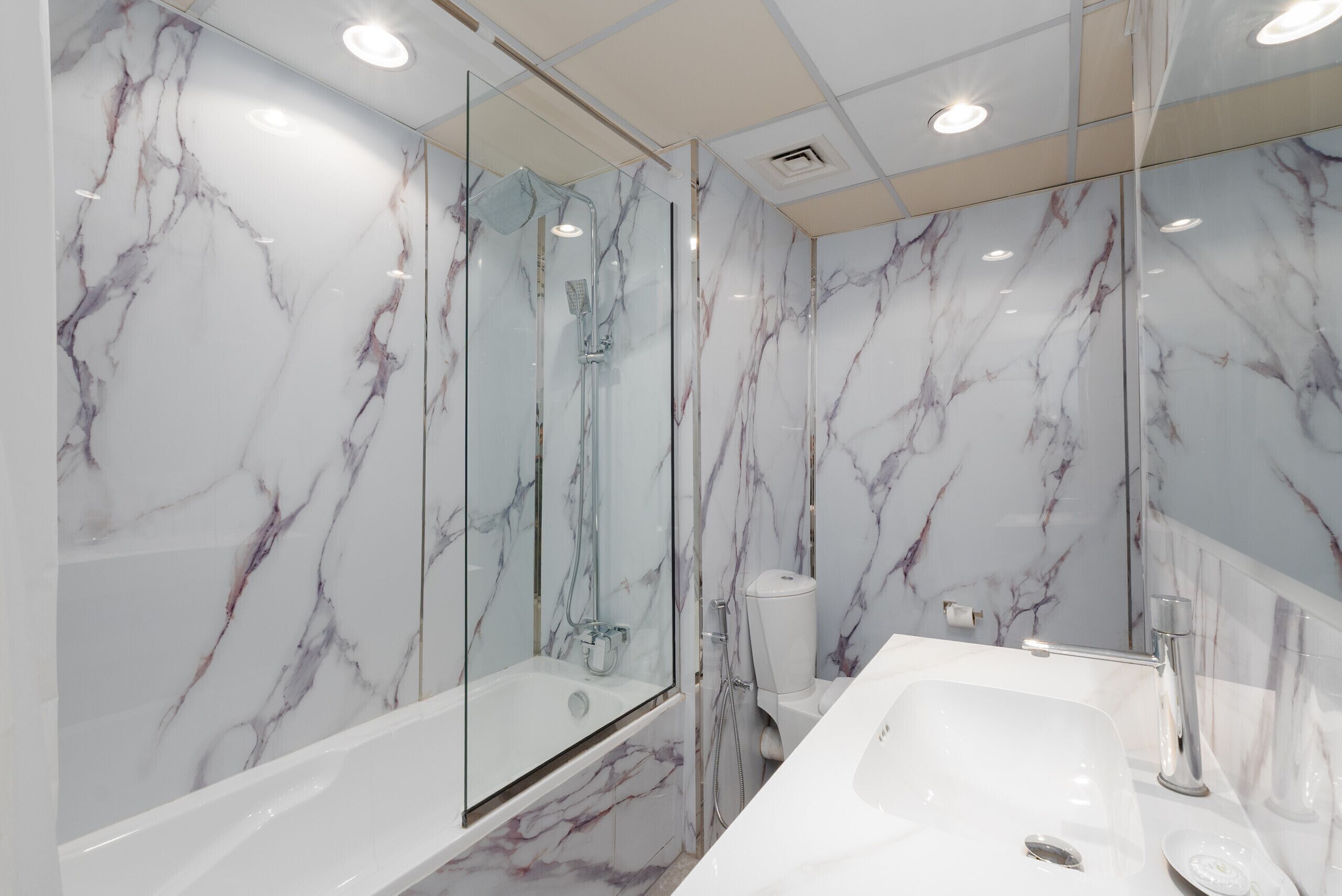 A modern bathroom with marble walls, a glass-enclosed shower, and a white sink.