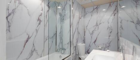 A modern bathroom with marble walls, a glass-enclosed shower, and a white sink.