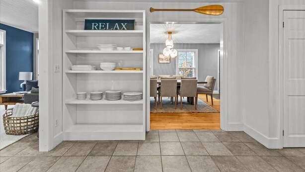 A modern interior with a white shelving unit labeled "RELAX" containing plates and bowls, leading to a dining area with a wooden floor and a dining table. - Stowe Valley Haven - Beautiful redesigned 4BR home (Stowe)