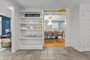 Un intérieur moderne avec une étagère blanche sur laquelle est inscrit le mot « RELAX », et qui contient des assiettes et des bols. Cette étagère donne sur un coin repas doté d’un plancher en bois et d’une table à manger.