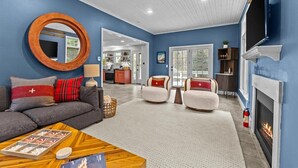 A living room with a fireplace, a round mirror, and a sofa with red and gray cushions. - Stowe Valley Haven - Beautiful redesigned 4BR home (Stowe)