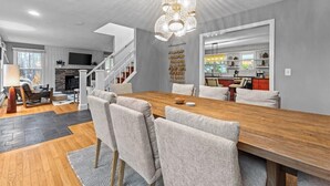 A modern dining area with a wooden table and chairs, a chandelier, and a staircase leading to another level. - Stowe Valley Haven - Beautiful redesigned 4BR home (Stowe)