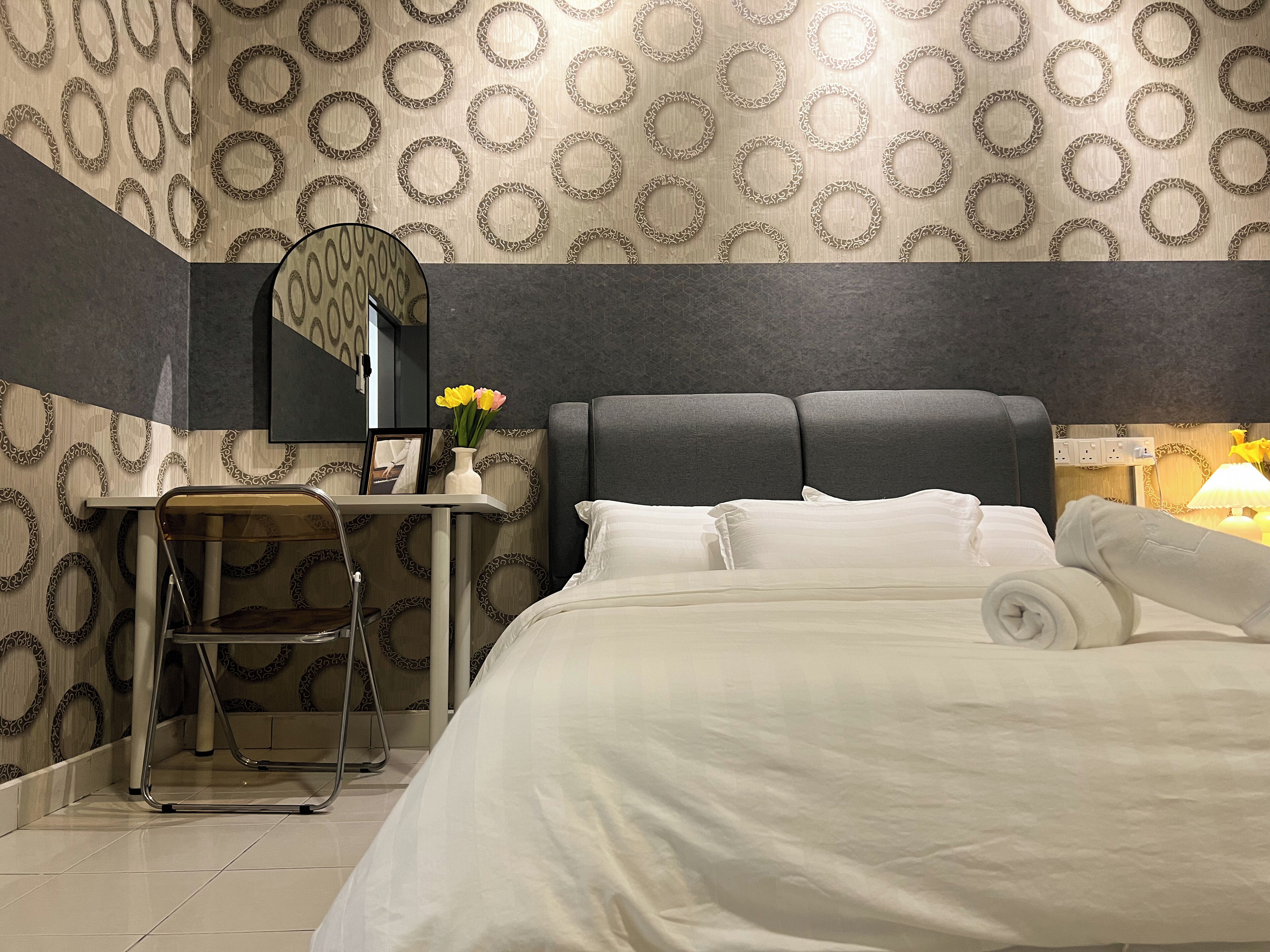 A hotel room with a bed, a desk, a chair, a mirror, and a nightstand with a lamp.