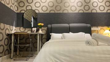 A hotel room with a bed, a desk, a chair, a mirror, and a nightstand with a lamp.