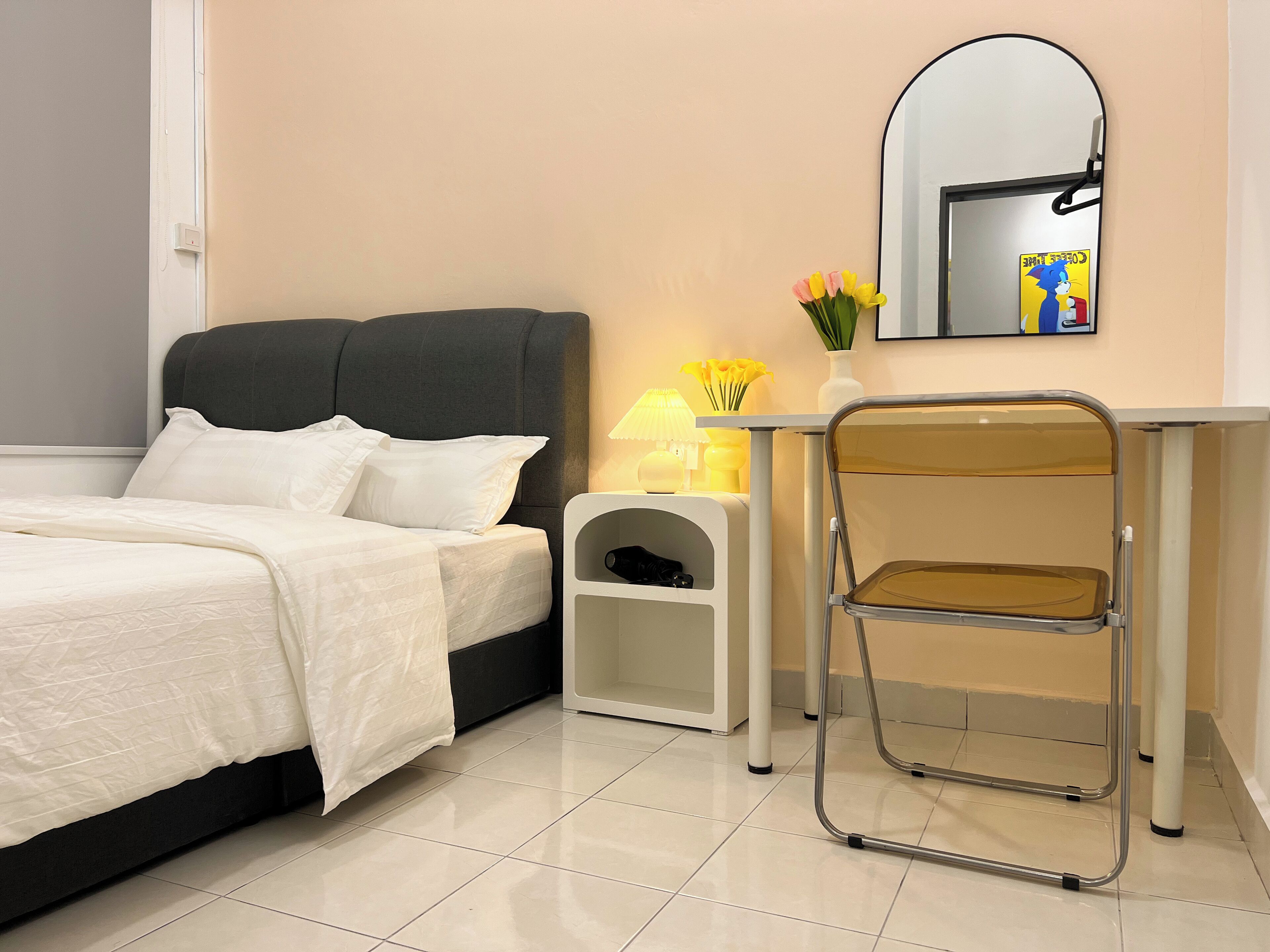 Un dormitorio ordenado con cama, mesita de noche, lámpara y una silla.