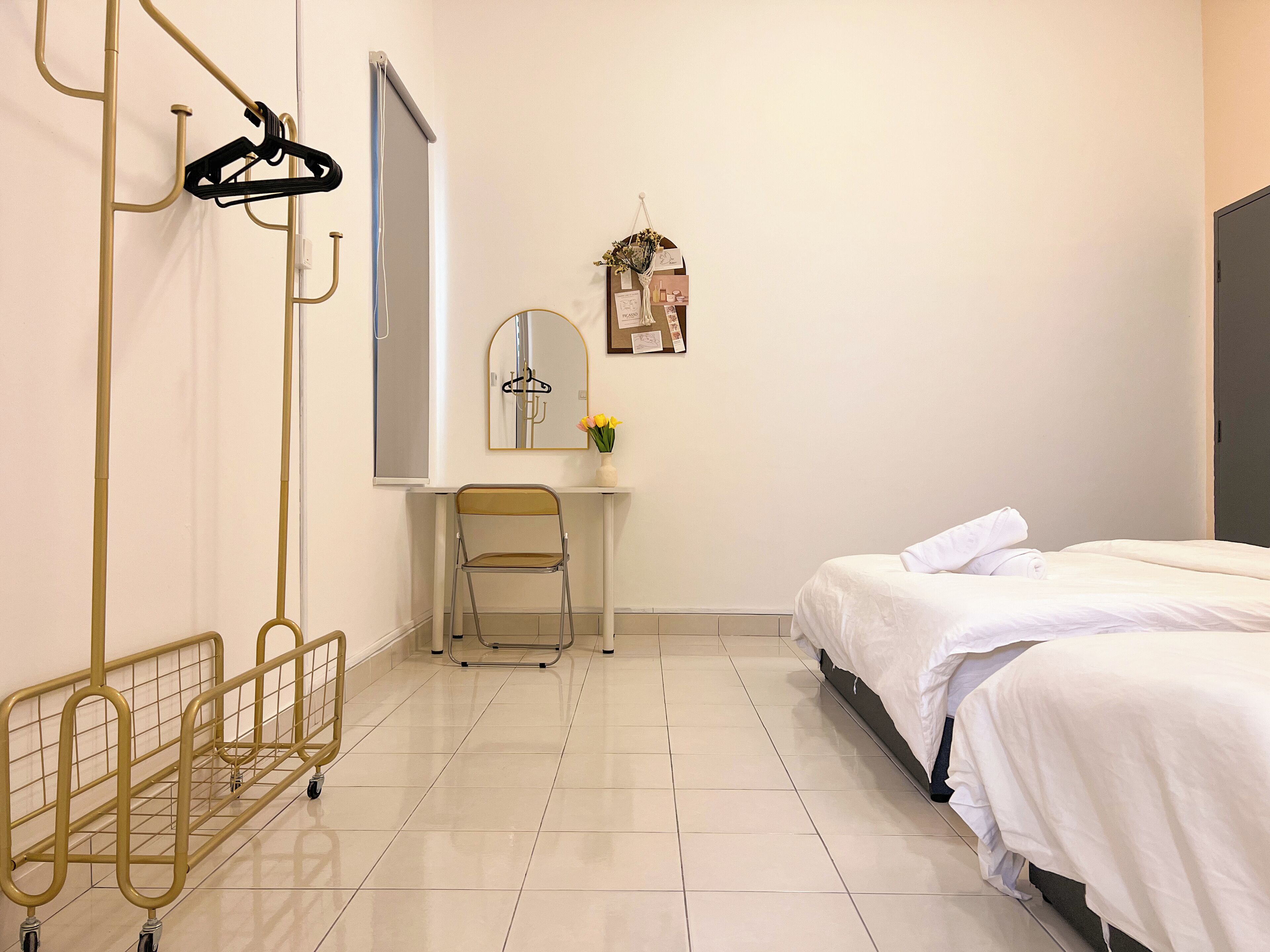 A hotel room with a bed, a desk, a chair, a mirror, a wall-mounted shelf with a vase, and a metal cart.