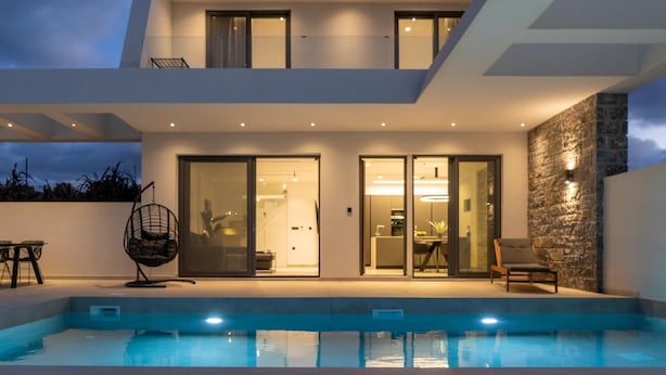 Et moderne hus med to etager, en swimmingpool, store skydedøre og en stenvæg som detalje.