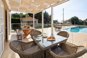 Une terrasse extérieure avec des meubles en osier, une table en verre et une piscine.
