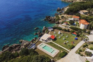 An aerial view of a coastal property with a swimming pool, a small boat, and a gazebo.