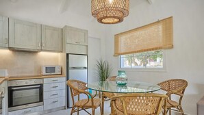 A modern kitchen with white cabinets, stainless steel appliances, and a glass dining table surrounded by wicker chairs. - Villa Artemis Periyali (Zakynthos)