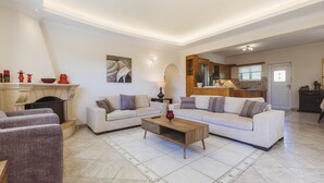 A spacious living room with a fireplace, two sofas, a coffee table, and a kitchen in the background. - Villa Lilly with private pool (Zakynthos)