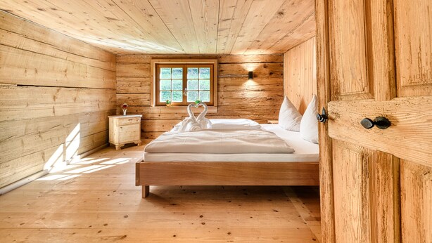 A wooden cabin bedroom with a bed, nightstand, and window. - Mountain house "Lutzklang" (Raggal)