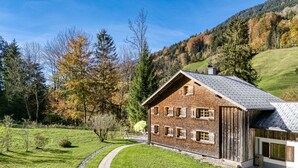 A rustic wooden house with a sloped roof, surrounded by a well-maintained lawn and trees. - Mountain house "Lutzklang" (Raggal)