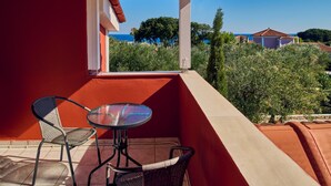 Ein Balkon mit Tisch und zwei Stühlen, mit Blick auf einen üppigen Garten und die Küste.