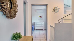 Ein Flur mit weißer Wand, einer dekorativen Wandgestaltung, einem kleinen Topfpflanzen und einer Treppe mit Geländer.
