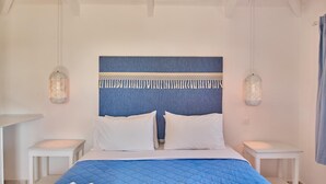 Ein Schlafzimmer mit einer blau gesteppten Bettdecke, weißen Kissen, einem blauen Kopfstück mit Quasten und zwei Nachttischen mit Lampen.