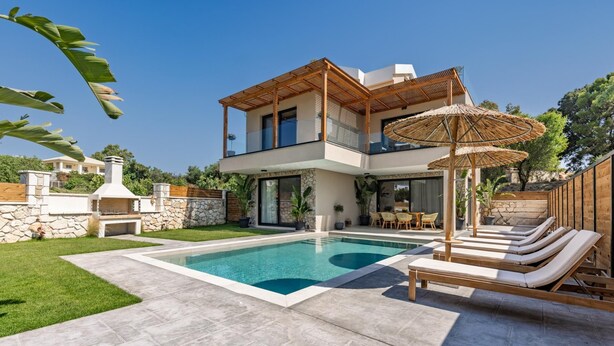 Una casa moderna de dos pisos con piscina, mobiliario exterior y un muro de piedra.
