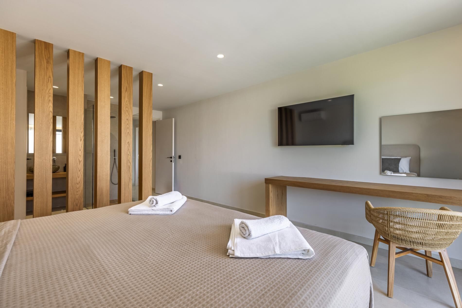 A modern hotel room with a large bed, a wooden partition, a television, and a wicker chair.