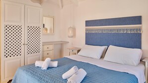 Una cama bien hecha con un edredón azul, almohadas blancas y toallas enrolladas.