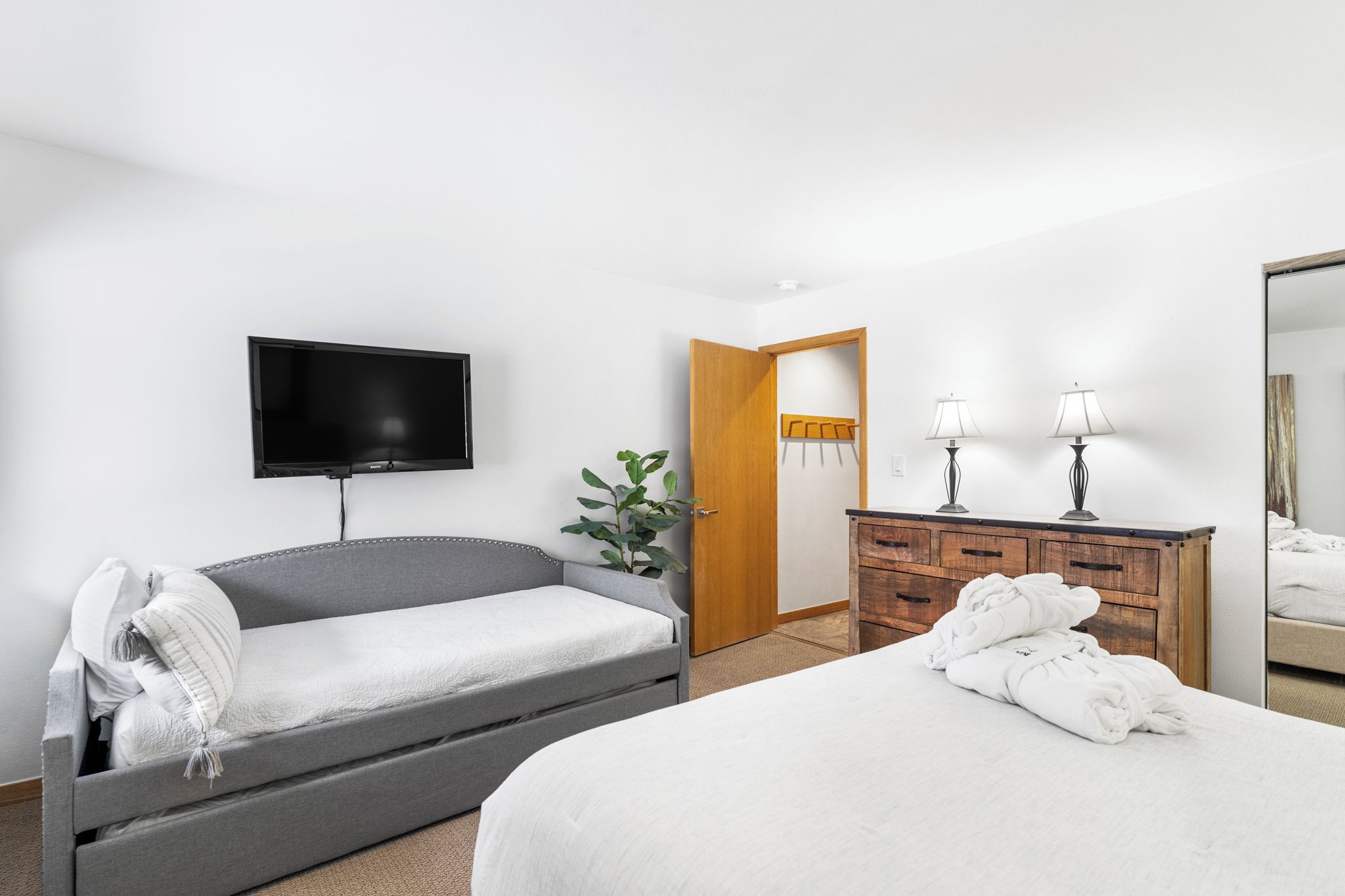 Une chambre comprenant un lit, un canapé-lit, une télévision, une commode et une porte donnant sur une autre pièce.