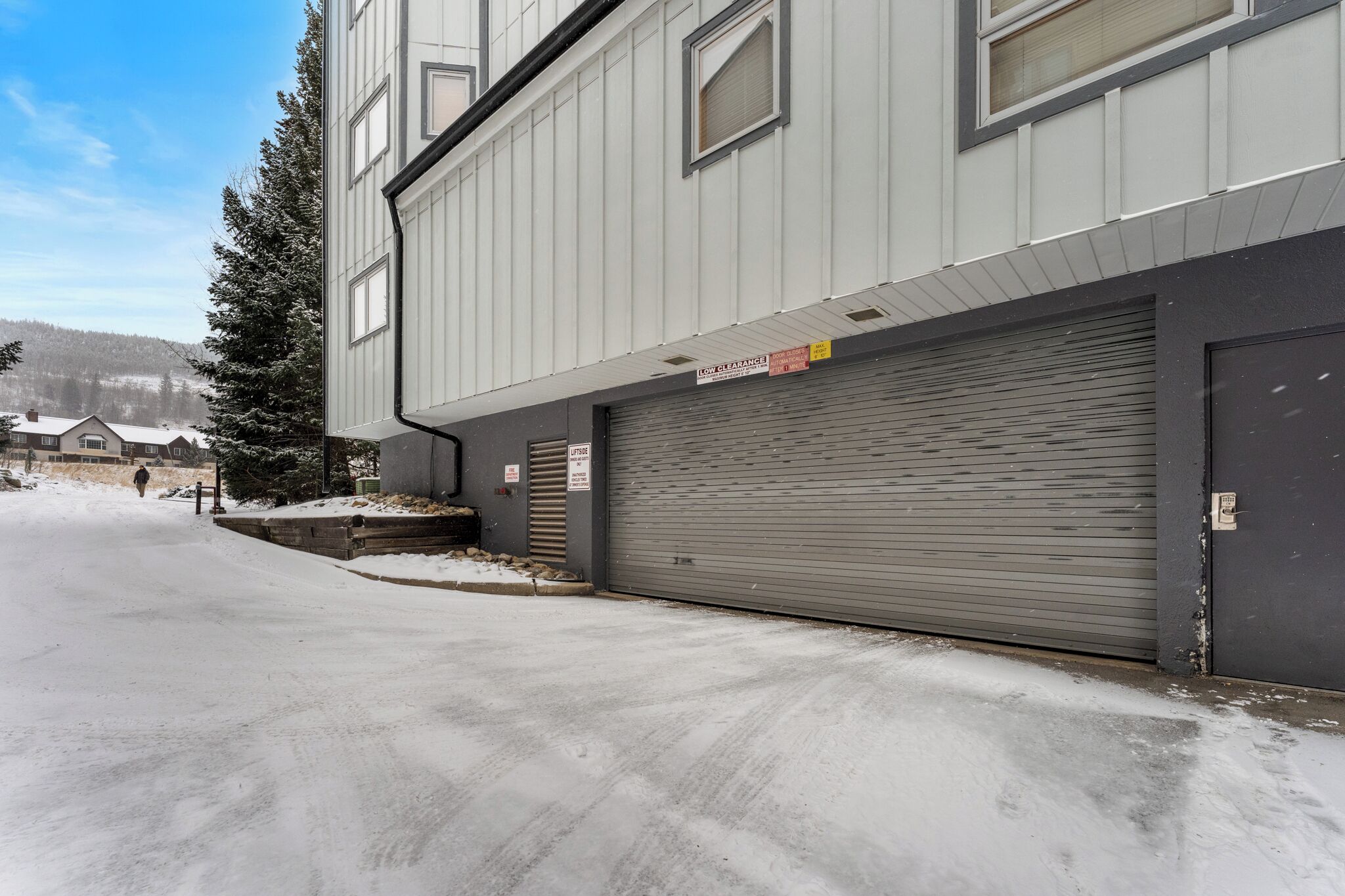 Un bâtiment avec une porte de garage fermée, un panneau indiquant une hauteur libre limitée et un sol recouvert de neige.