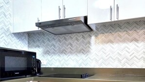 A modern kitchen with white cabinets, a built-in microwave, and a stainless steel range hood.