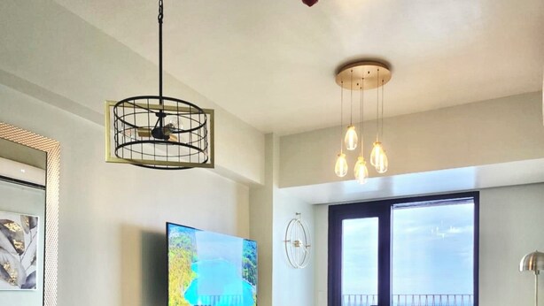 A modern living room with a large TV, a dining area with chairs, and a balcony with a view.