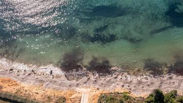 Vue aérienne d’une zone côtière caractérisée par une eau claire, un littoral rocheux et un sentier étroit menant à la plage.