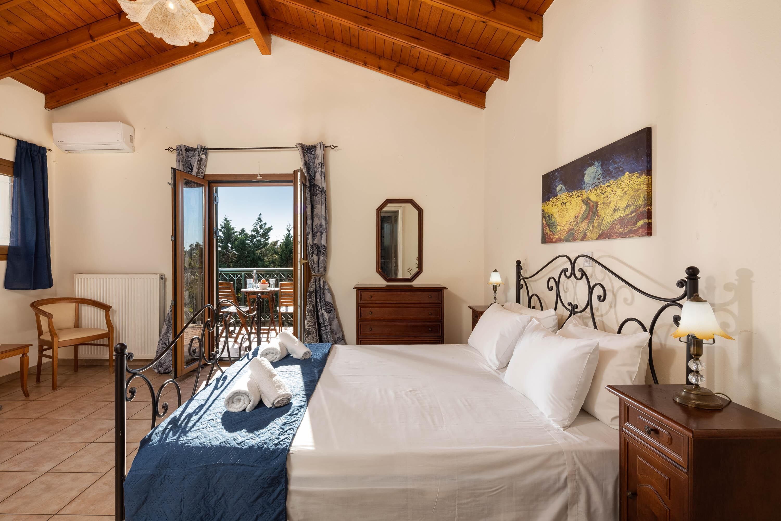 Une chambre d’hôtel comprenant un lit, une table de chevet, une lampe, un tableau, un miroir, une fenêtre avec des rideaux, une chaise, une table et un appareil de climatisation.