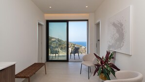 Une chambre moderne dotée d’une grande porte-fenêtre coulissante qui donne sur un balcon offrant une vue sur la mer. On y trouve un banc, une chaise et un pot de fleurs.