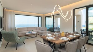 Un salon moderne avec un coin repas, de grandes fenêtres et une vue sur la mer.