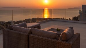 Un balcon doté de meubles en osier et offrant une vue sur le coucher de soleil sur la mer.