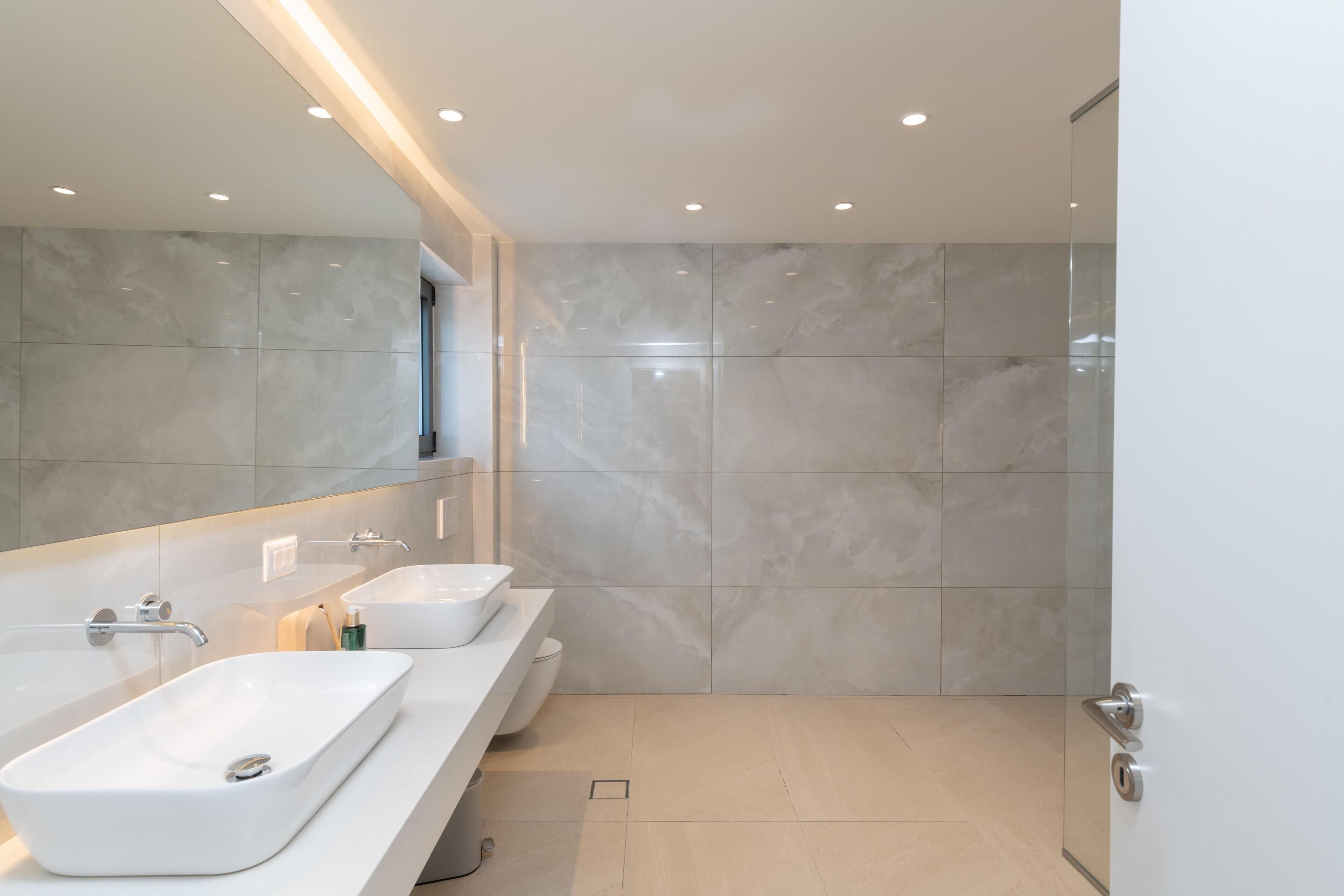 A modern bathroom with a large mirror, two sinks, and a shower area.