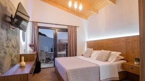 Une chambre à coucher comprenant un lit, une tête de lit en bois, un téléviseur fixé au mur et une porte-fenêtre coulissante donnant sur un espace extérieur.