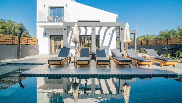 Une maison moderne à deux étages dotée d’une piscine, de chaises longues et d’une pergola avec des parasols.