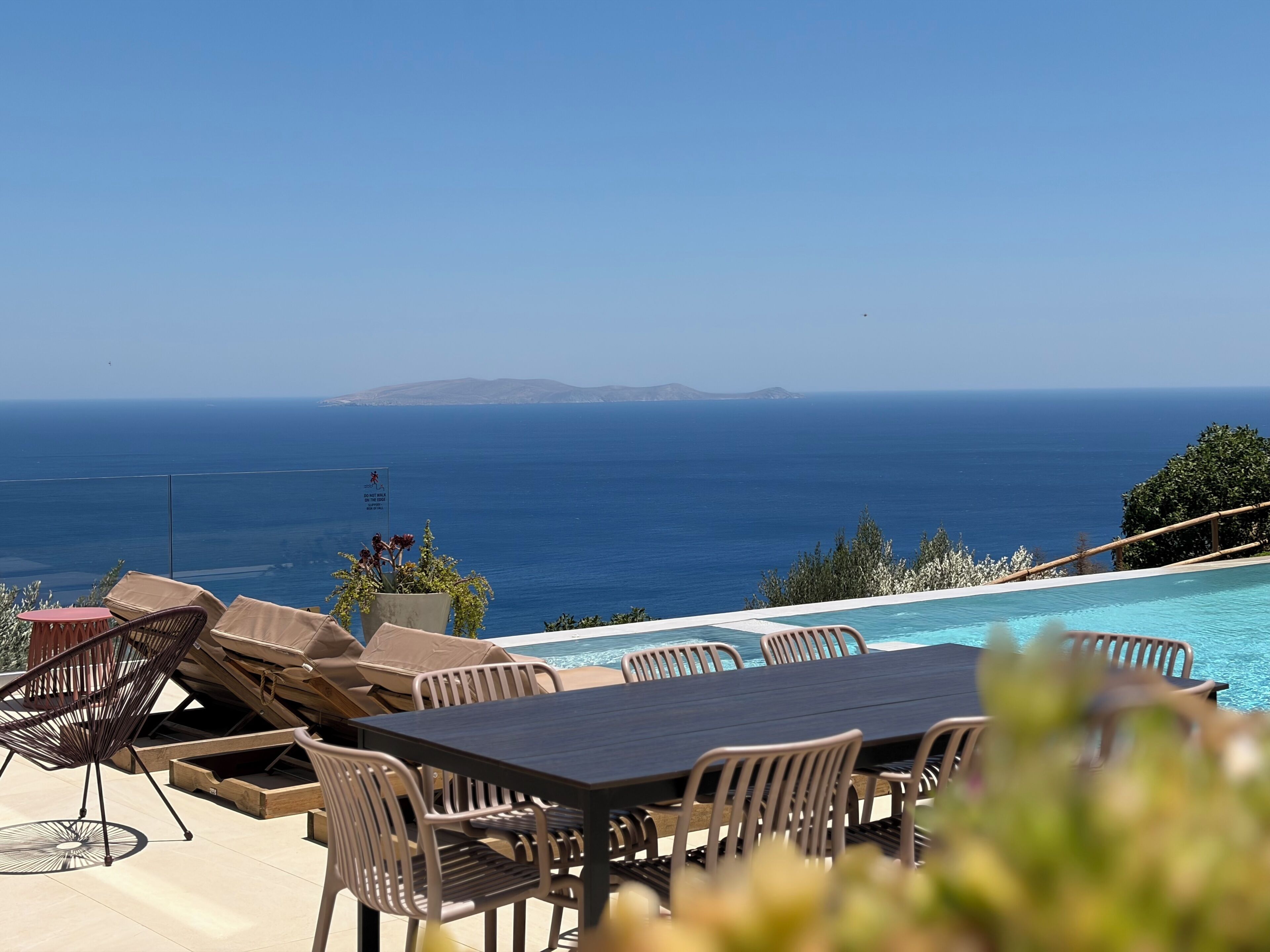 A poolside area with lounge chairs, a table, and a view of the ocean.