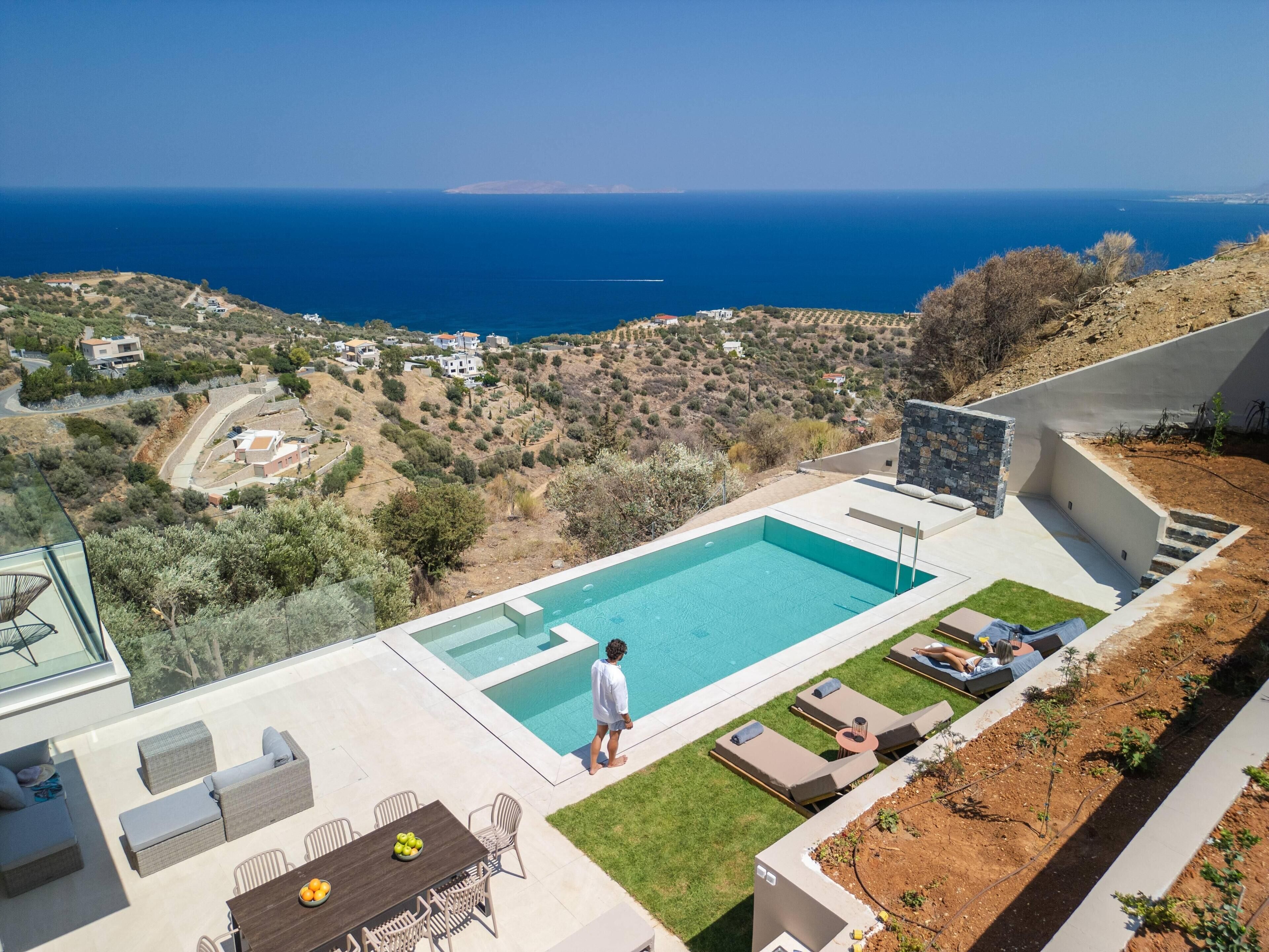 Un área de piscina moderna al aire libre con vista al mar y un paisaje montañoso.