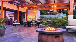 An outdoor dining area with tables and chairs, a fire pit, and potted plants.