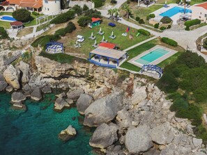 Vue aérienne d’une propriété située sur la côte, avec une piscine, un patio couvert et un terrain rocheux.